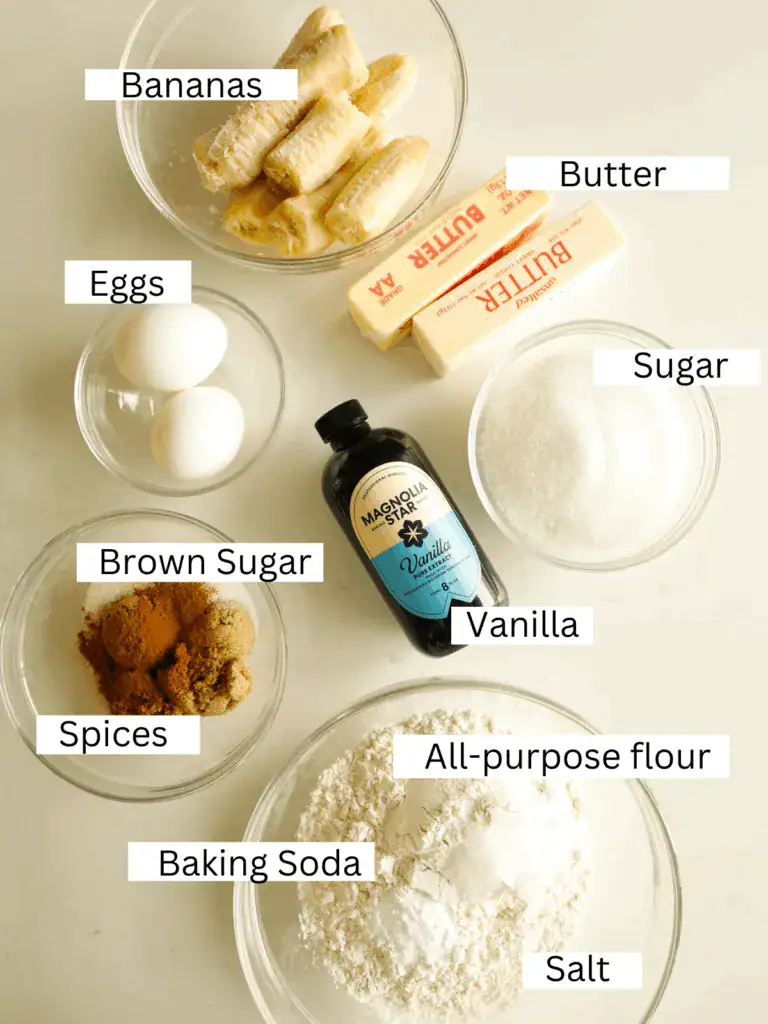Ingredients for cinnamon banana bread including bananas, butter, eggs, sugars, vanilla, flour, spices, and leaveners displayed in glass bowls.