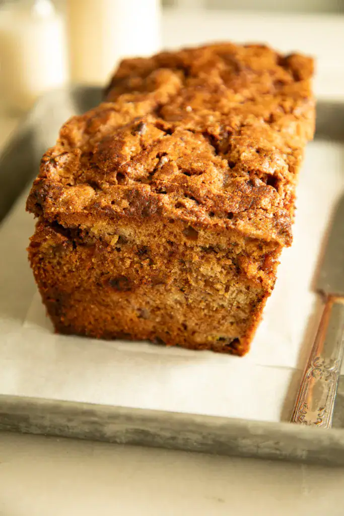 Freshly baked cinnamon banana bread loaf on parchment-lined metal tray with butter knife.