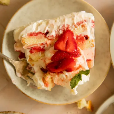 Slice of icebox cake on a plate with a fork digging in, showing creamy texture and vibrant strawberry topping.