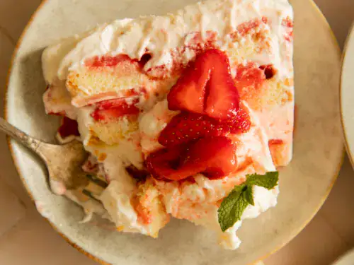 Slice of icebox cake on a plate with a fork digging in, showing creamy texture and vibrant strawberry topping.