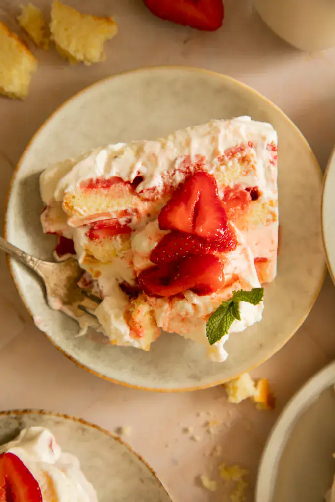 Slice of icebox cake on a plate with a fork digging in, showing creamy texture and vibrant strawberry topping.