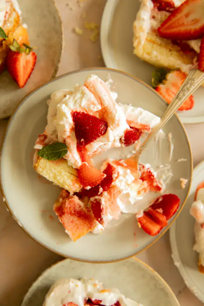 Partially eaten slice of strawberry icebox cake on a plate, showing whipped cream and juicy strawberries.