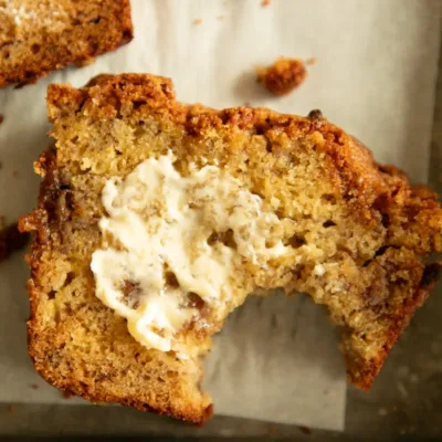 Close-up of a slice of banana bread with a bite taken out and melted butter on top.