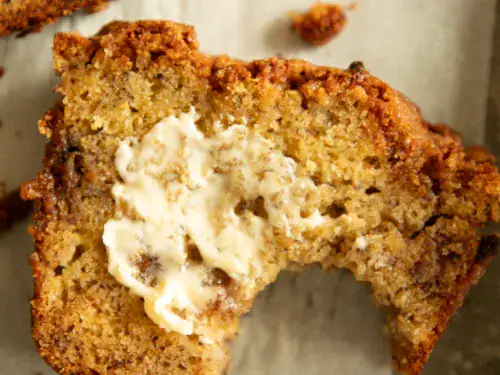 Close-up of a slice of banana bread with a bite taken out and melted butter on top.