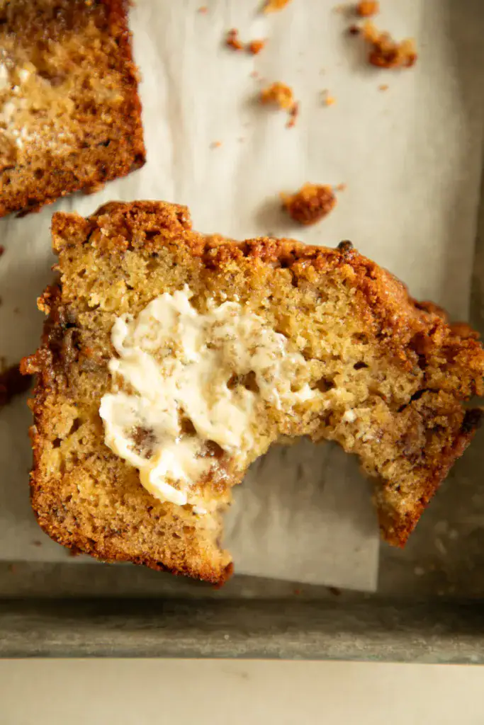 Close-up of a slice of banana bread with a bite taken out and melted butter on top.