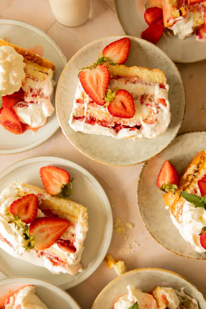 Multiple slices of strawberry shortcake icebox cake served on ceramic plates, styled with berries and whipped cream.