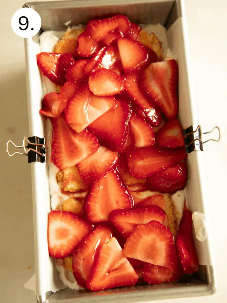 Loaf pan filled with strawberry shortcake icebox cake, smoothed over with a final whipped cream layer.