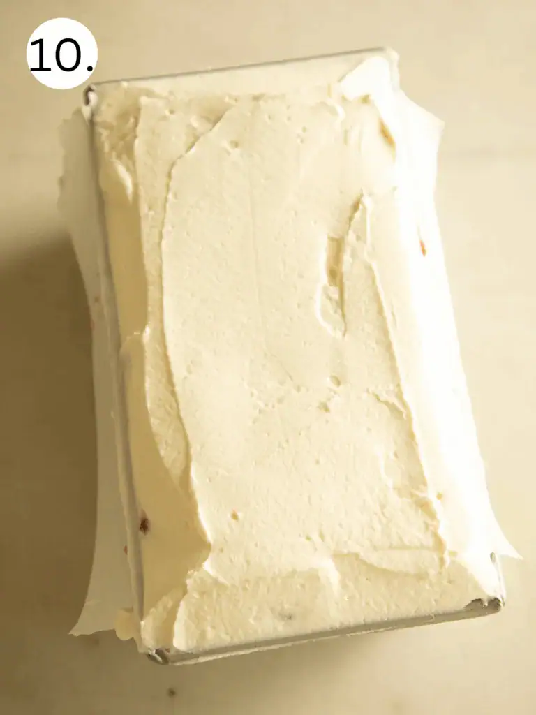 Loaf pan filled with strawberry shortcake icebox cake, smoothed over with a final whipped cream layer.