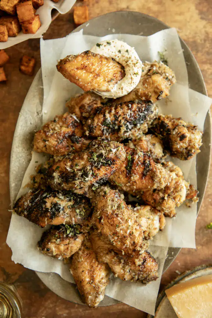 Crispy Cacio e Pepe wings on a parchment-lined platter topped with Pecorino Romano, served with creamy dipping sauce