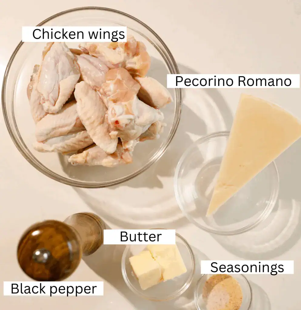 Overhead shot of raw chicken wings, Pecorino Romano, butter, seasonings, and black pepper in bowls