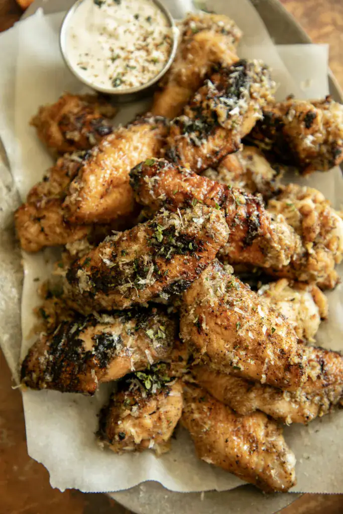 Crispy grilled chicken wing being dipped in creamy sauce, showing golden brown crust and cheese topping