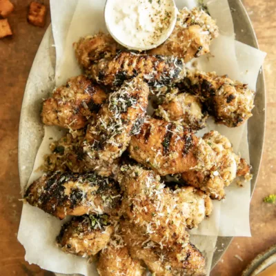 Wide overhead view of grilled wings on a platter with dipping sauce, crispy sweet potatoes on the side