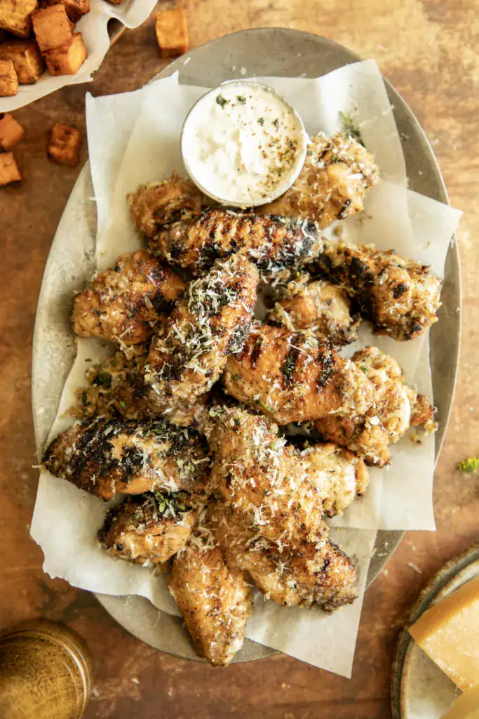 Wide overhead view of grilled wings on a platter with dipping sauce, crispy sweet potatoes on the side