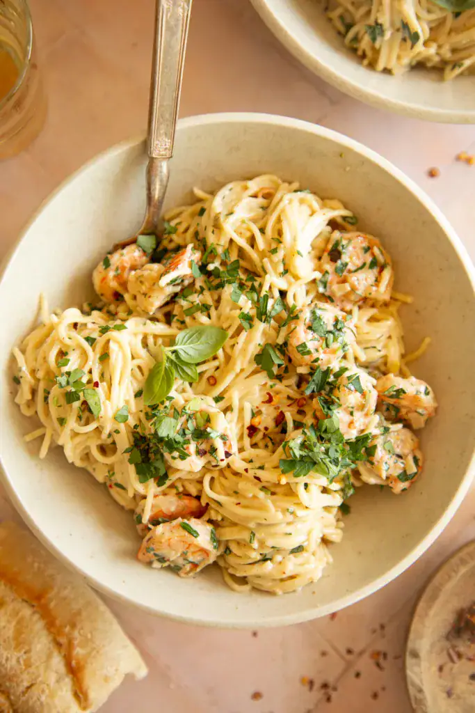 Close-up of shrimp scampi pasta served in a bowl with fresh herbs and red pepper flakes.