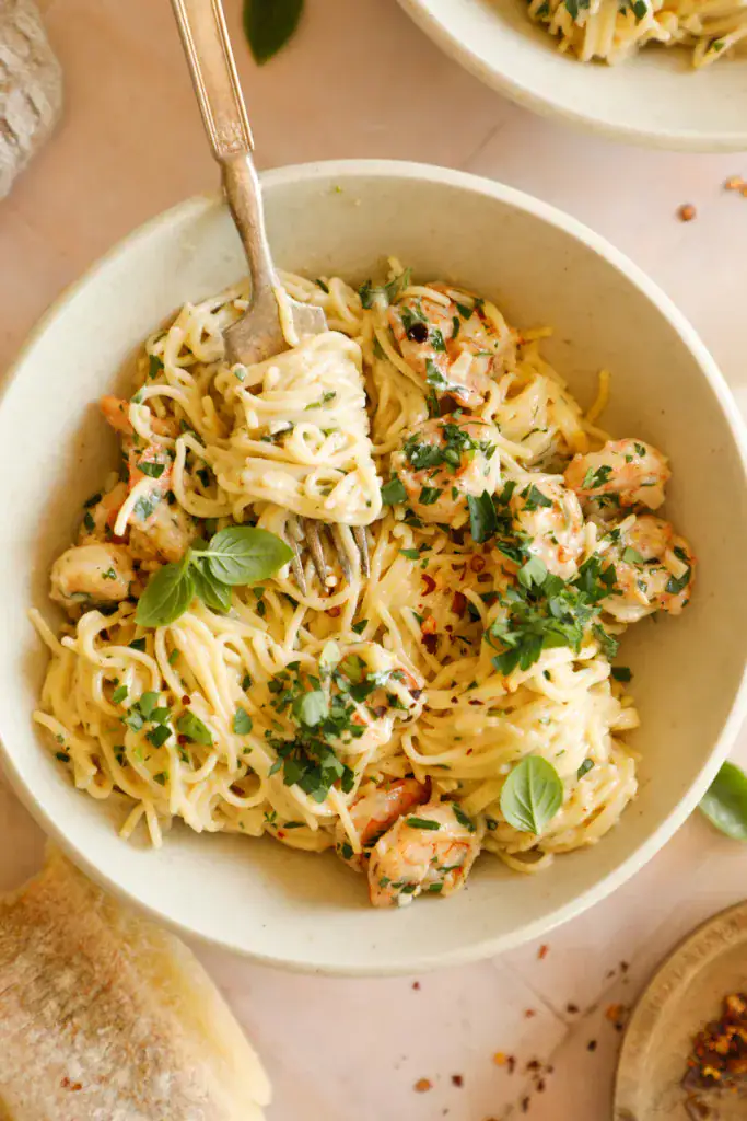 Fork twirling creamy shrimp scampi pasta with fresh herbs in a shallow bowl.
