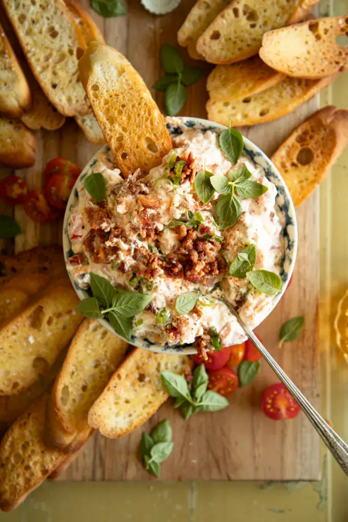 Close-up of BLT dip in a blue patterned bowl with bacon, green onion, and basil leaves