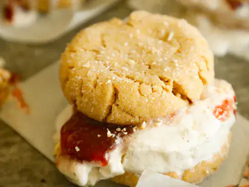 Close-up of a peanut butter and jelly ice cream sandwich with cracked cookie tops and chopped peanuts