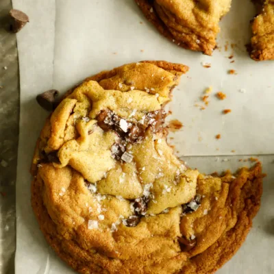 Gooey chocolate chip cookie with a bite taken out, sprinkled with flaky sea salt.