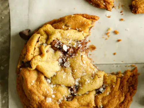 Gooey chocolate chip cookie with a bite taken out, sprinkled with flaky sea salt.