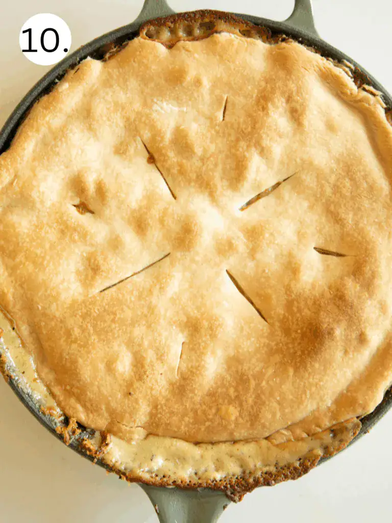 Golden brown baked pot pie in skillet with slightly bubbly edges and slits cut into the crust.