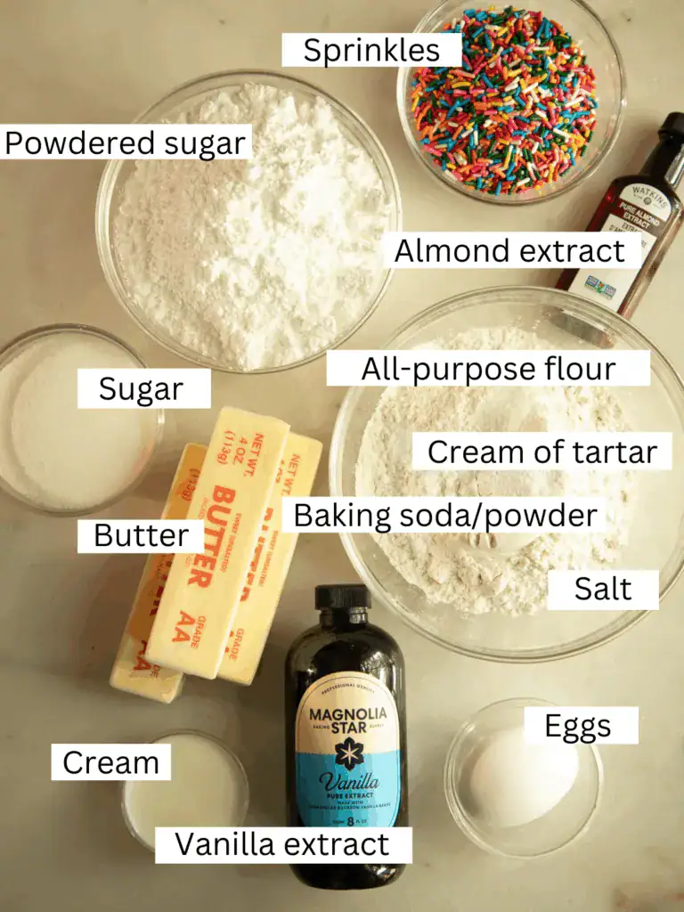 Overhead shot of labeled ingredients for funfetti shortbread cookie sandwiches, including butter, flour, sugar, sprinkles, and extracts.