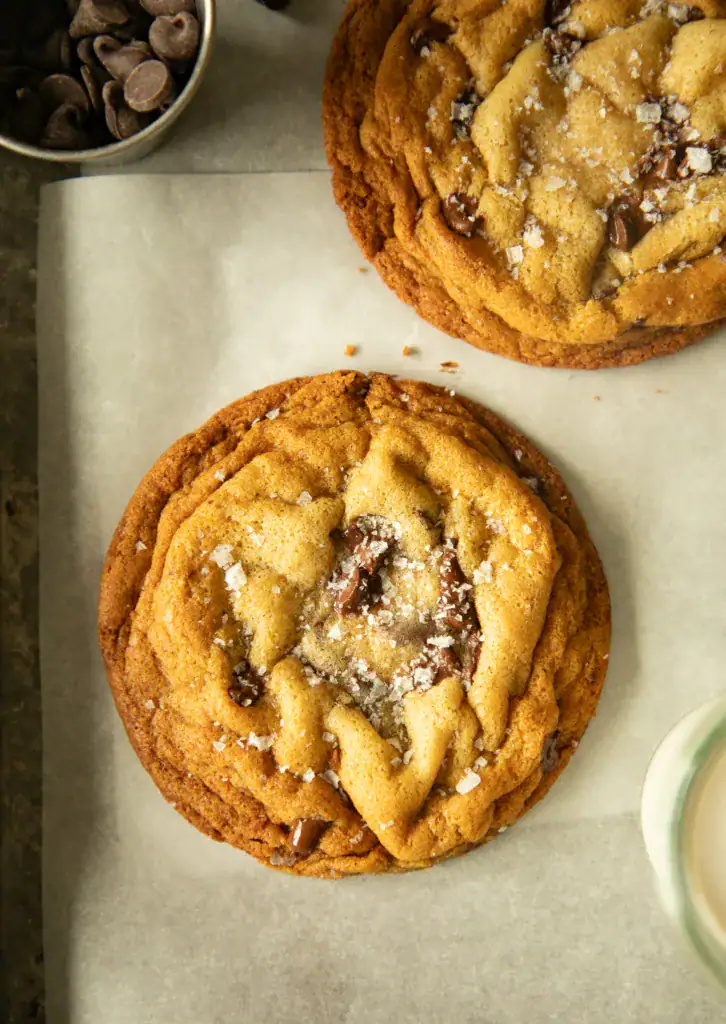 Two golden brown chocolate chip cookies with melted centers and flaky salt.