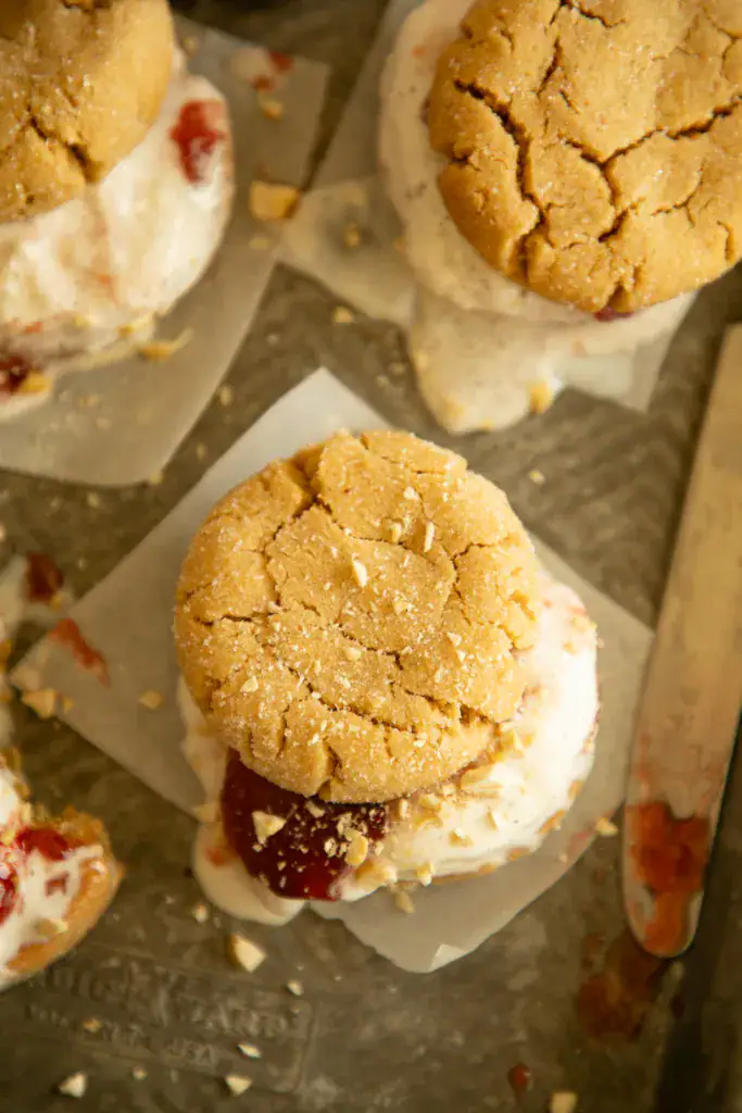 Side view of a peanut butter ice cream sandwich with strawberry jelly and vanilla ice cream melting at the edges