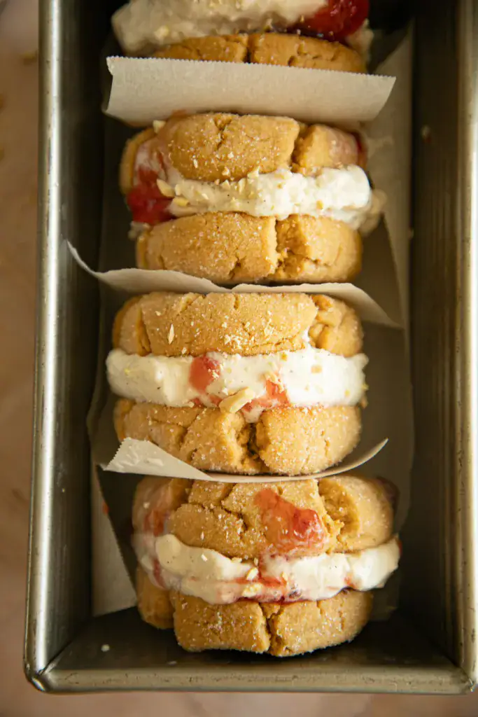 Four peanut butter and jelly ice cream sandwiches layered in a loaf pan with parchment paper between each sandwich
