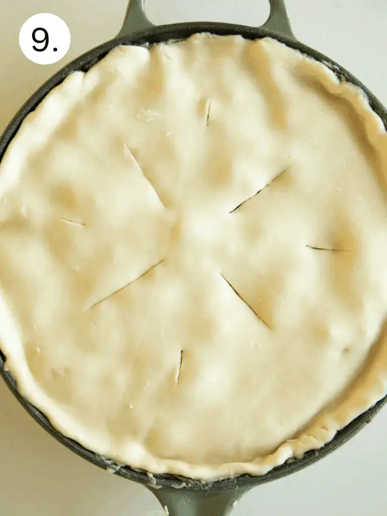 Creamy chicken Alfredo filling in skillet topped with unbaked pie crust, slits cut for steam release.