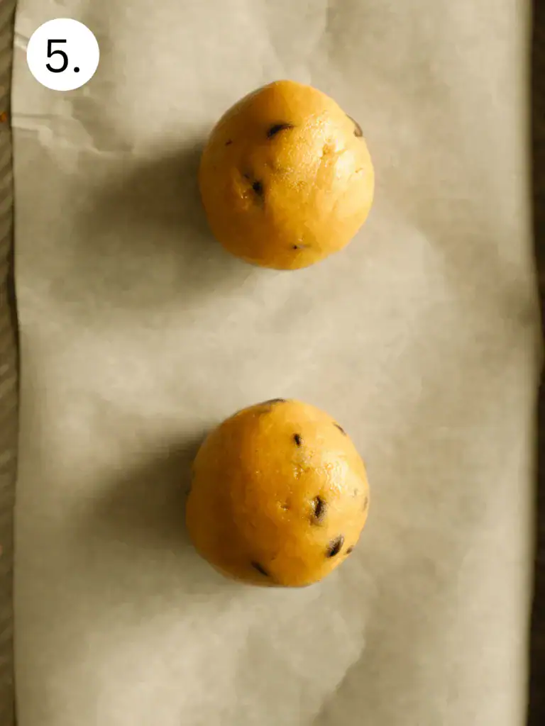 Two scooped cookie dough balls on parchment paper before baking.