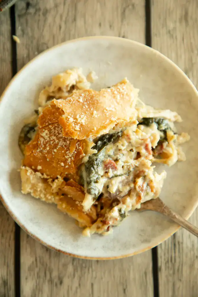 Plate with a generous serving of chicken Alfredo pot pie showing flaky crust, creamy filling, spinach, and bacon.