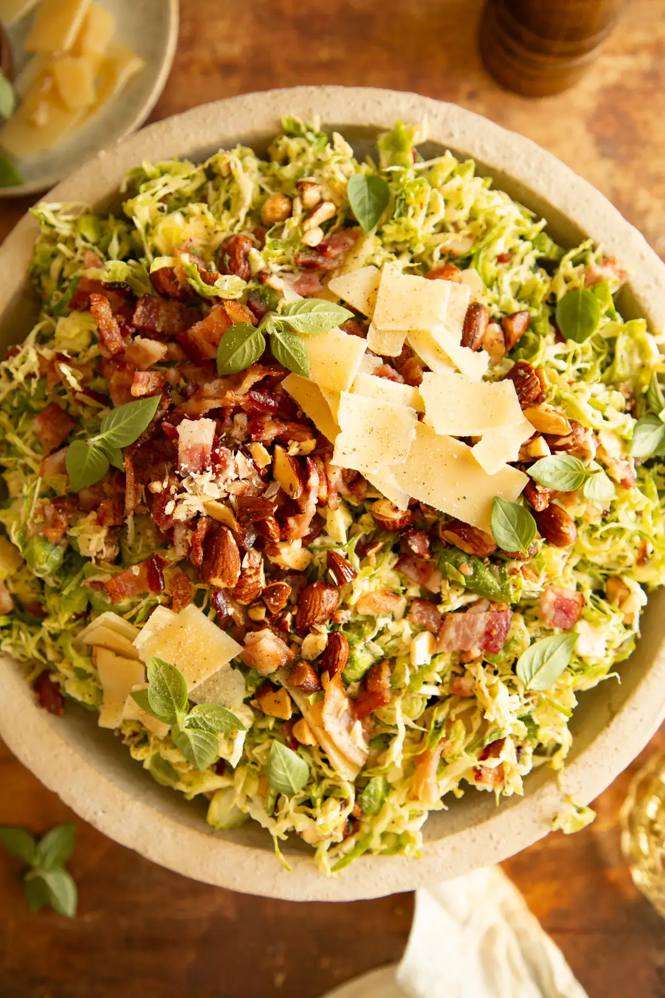 Overhead shot of Brussels sprout salad in a stone bowl, topped with chopped bacon, shaved parmesan, toasted almonds, and fresh herbs.
