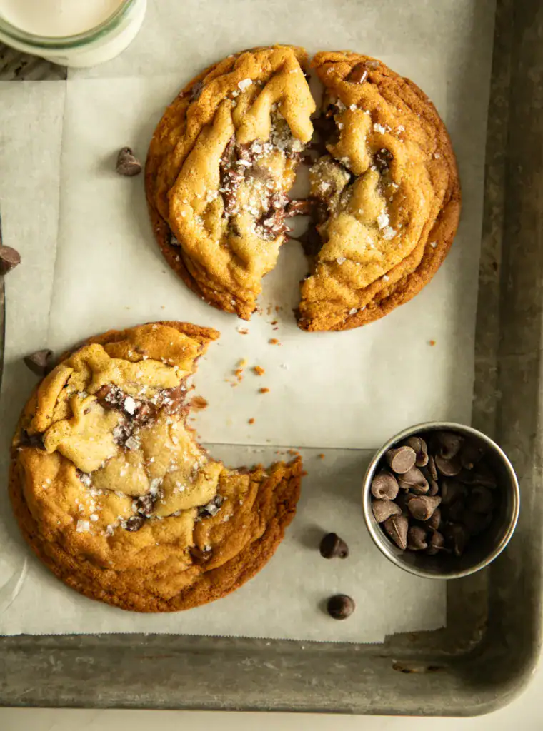 Close-up of two golden brown chocolate chip cookies sprinkled with flaky sea salt on parchment paper.