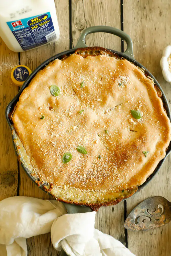 Skillet full of chicken Alfredo pot pie with rich creamy filling and golden Parmesan-topped crust, garnished with fresh herbs.