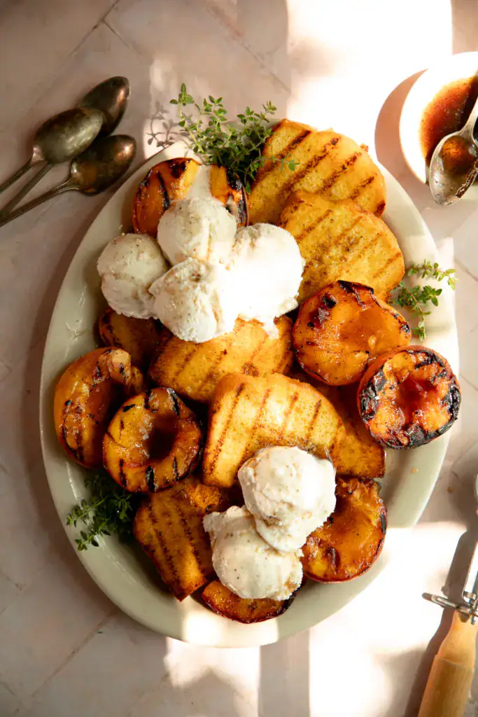 Grilled pound cake and peaches plated with scoops of vanilla ice cream and fresh thyme.