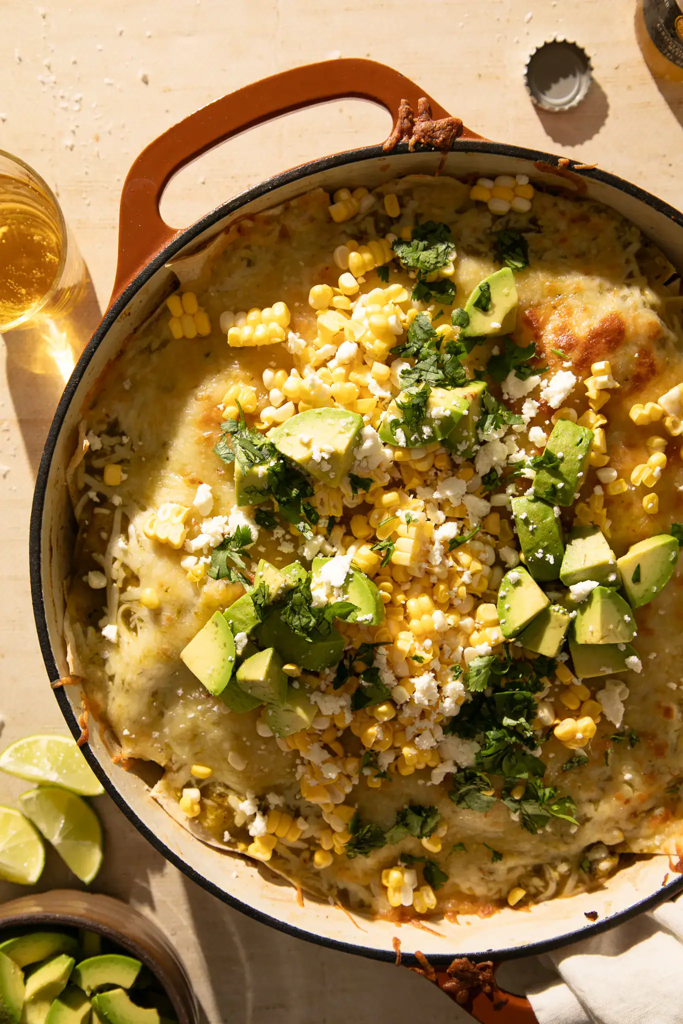 Close-up of a serving spoon scooping out a cheesy portion of green chile enchilada skillet topped with avocado, corn, and cilantro.