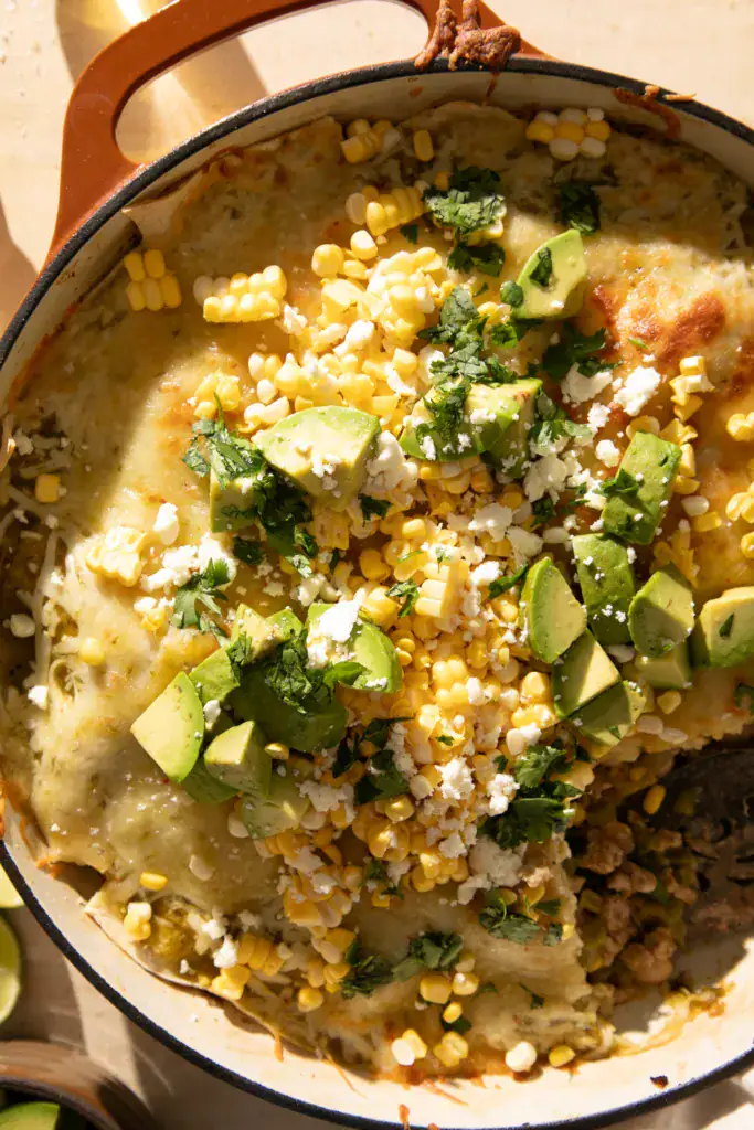 A scoop removed from the skillet reveals the cheesy green chile and ground turkey filling layered with beans, corn, and tortillas.