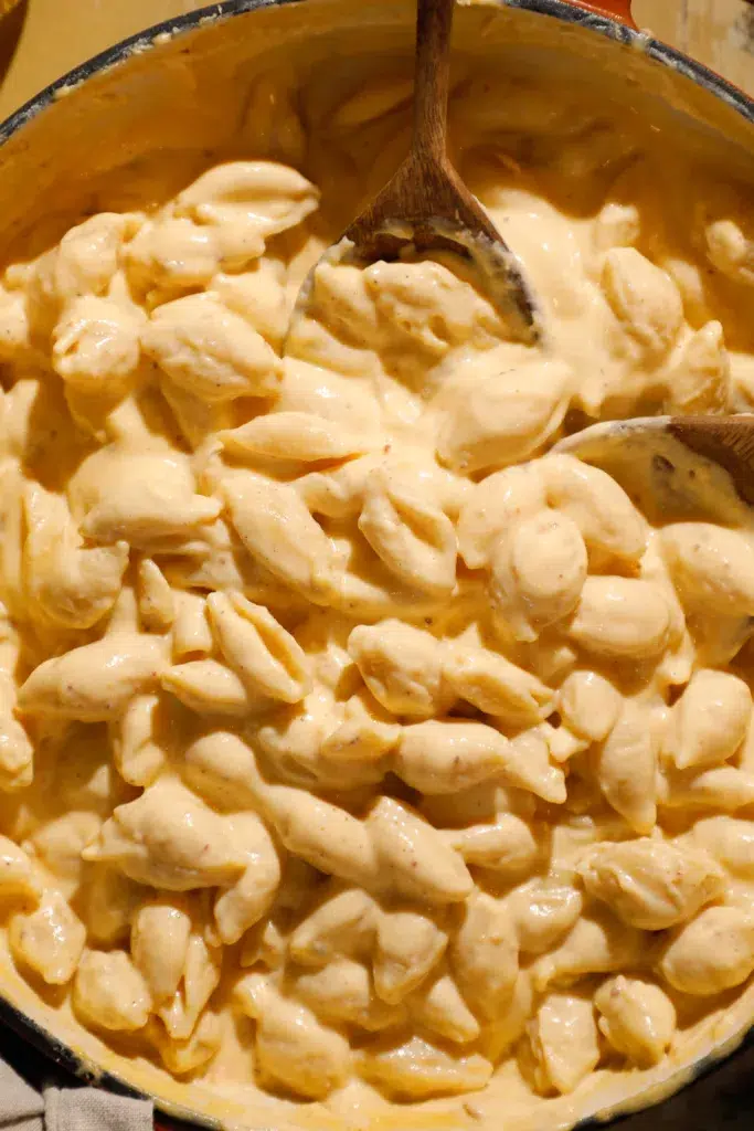 Overhead of a pot filled with cheesy pasta shells coated in thick sauce, stirred with a wooden spoon.