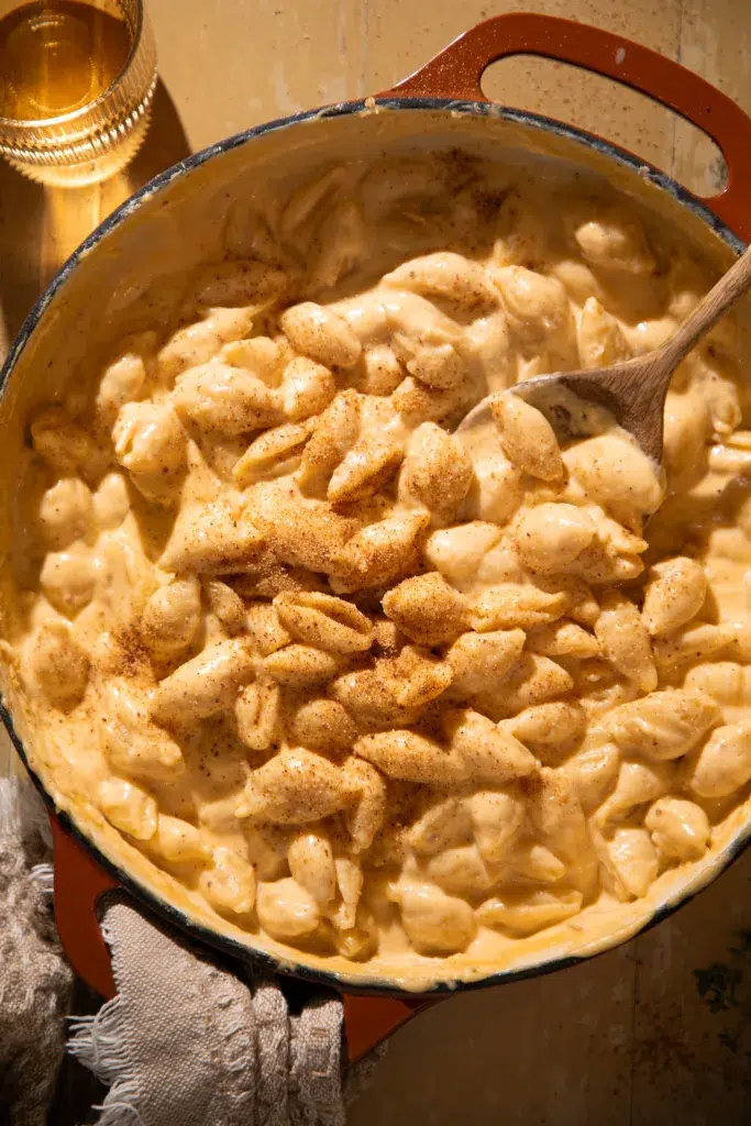 Creamy macaroni and cheese shells sprinkled with paprika in a Dutch oven with a wooden spoon.