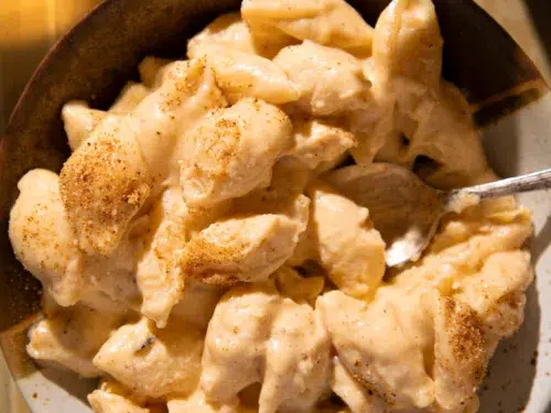 Serving of creamy shells and cheese in a rustic bowl with a spoon, topped with paprika.