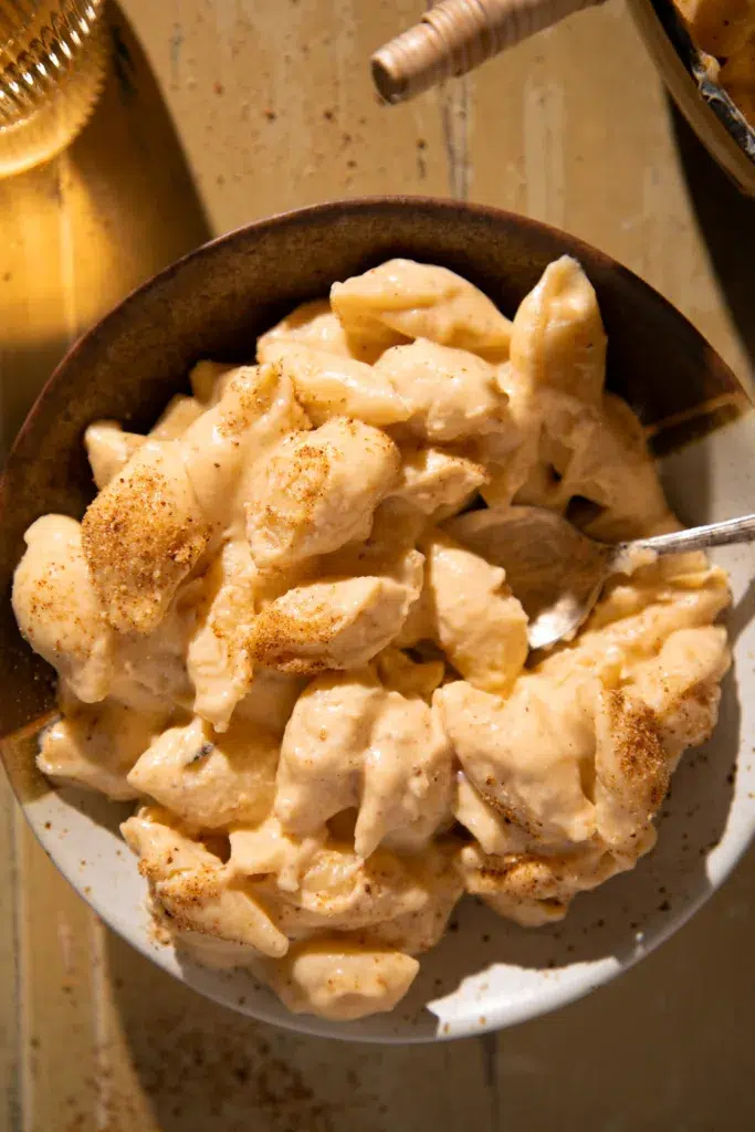 Serving of creamy shells and cheese in a rustic bowl with a spoon, topped with paprika.