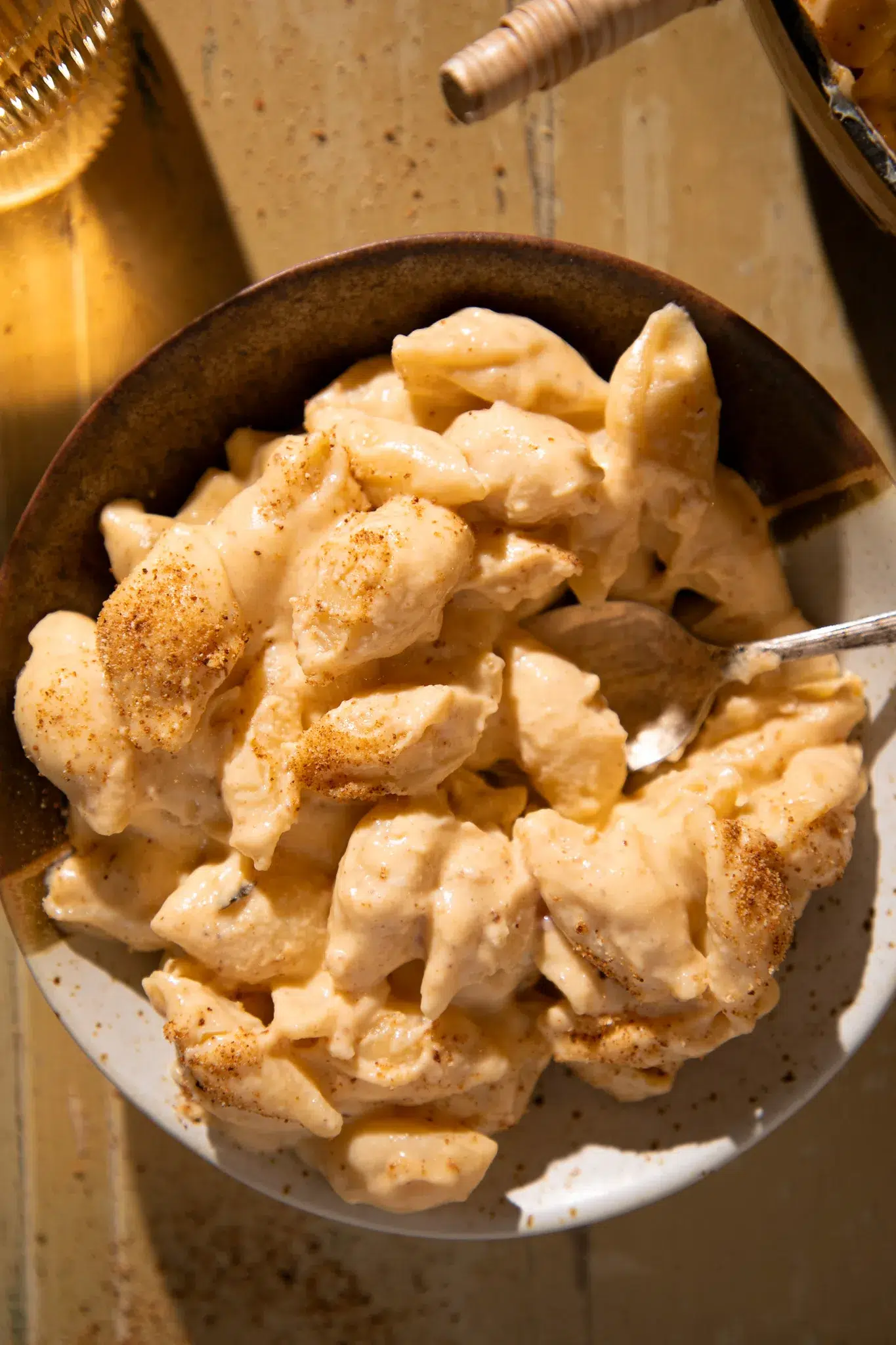 Serving of creamy shells and cheese in a rustic bowl with a spoon, topped with paprika.