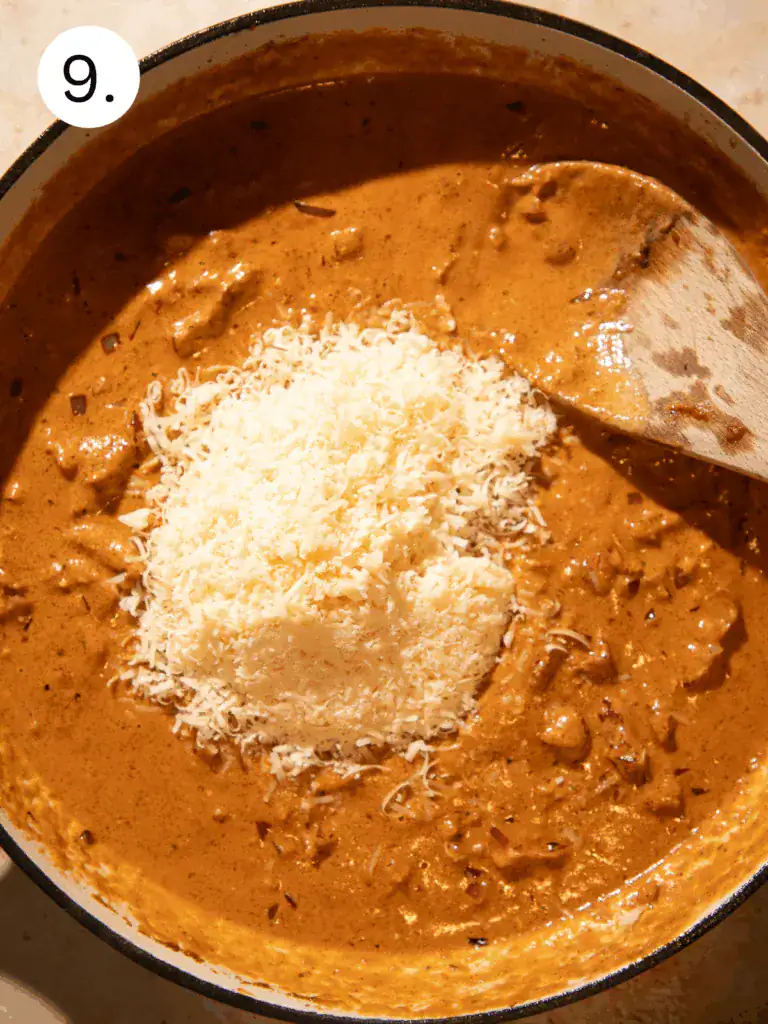 Freshly grated parmesan cheese melting into creamy sun-dried tomato sauce in a skillet.