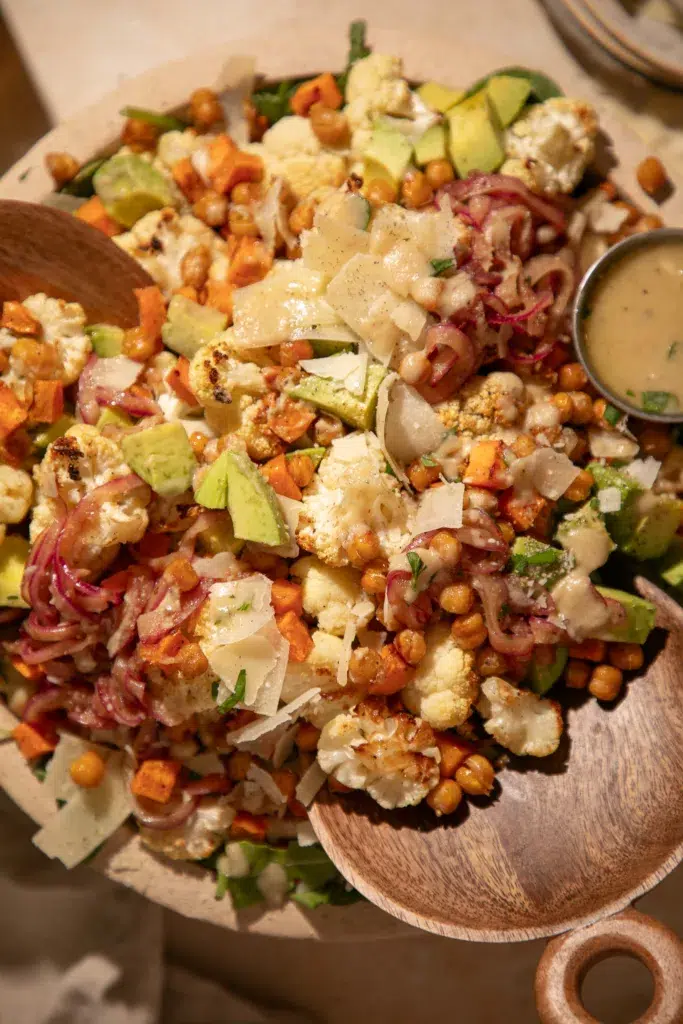 Close-up of roasted cauliflower salad showing crispy chickpeas, avocado slices, parmesan, and fresh arugula.