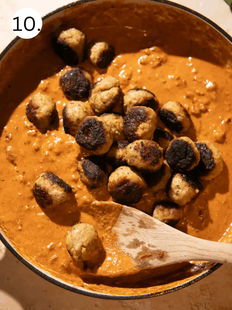 Golden-browned chicken meatballs simmering in creamy sun-dried tomato sauce in a skillet.