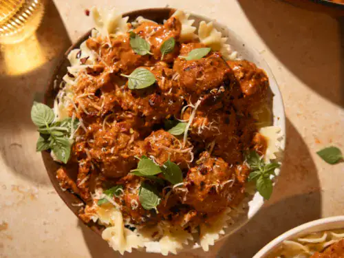 Bowl of bowtie pasta topped with creamy pesto marry me chicken meatballs and fresh basil.