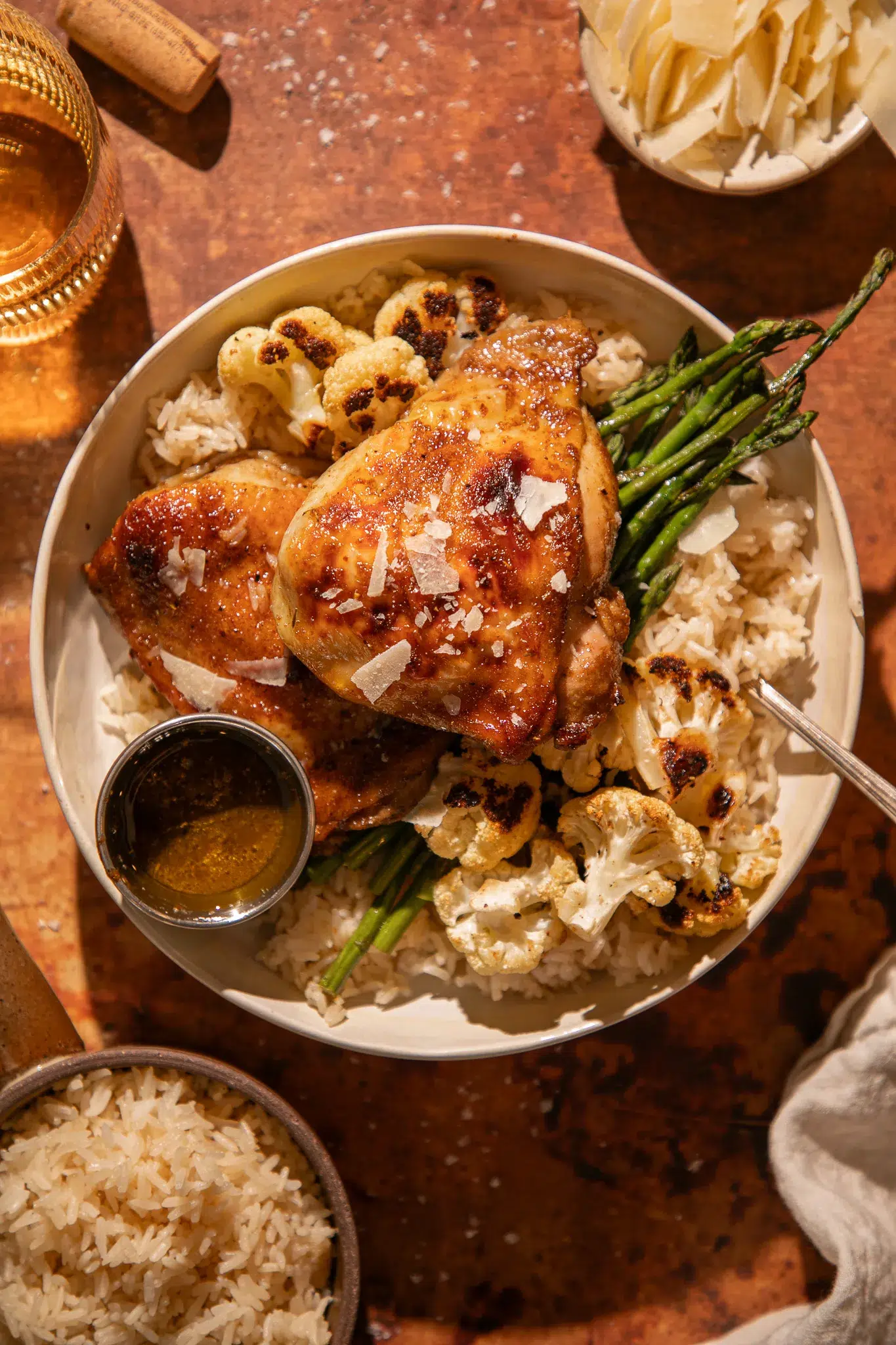 Overhead view of roasted chicken thighs, cauliflower, and asparagus over rice, garnished with parmesan and balsamic glaze.