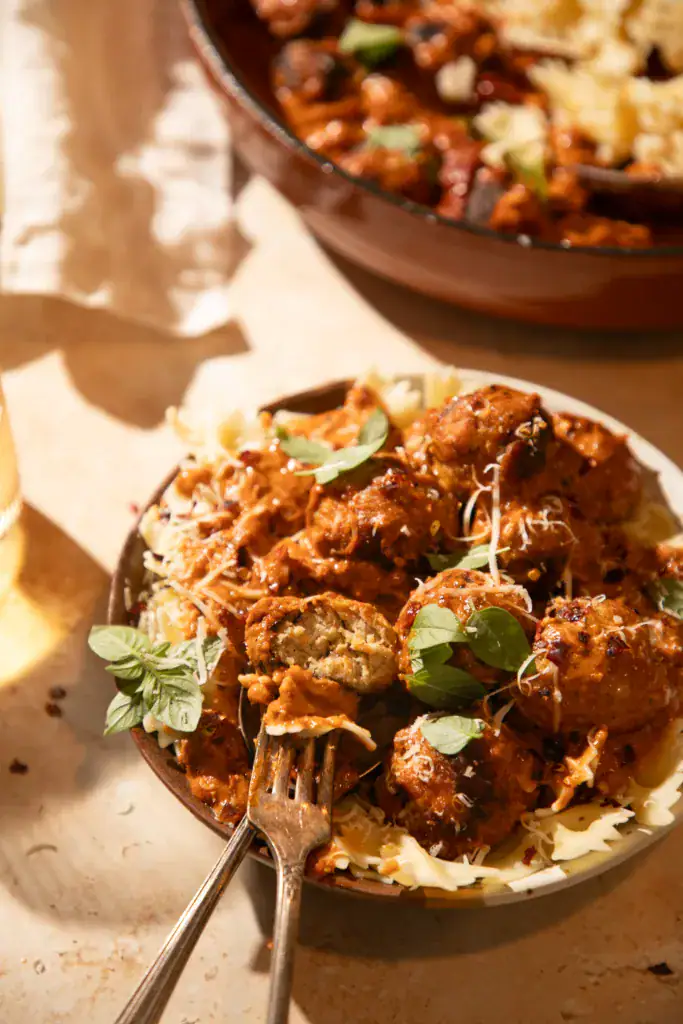 Bowl of creamy pesto marry me chicken meatballs with pasta, one meatball cut open to show juicy inside.