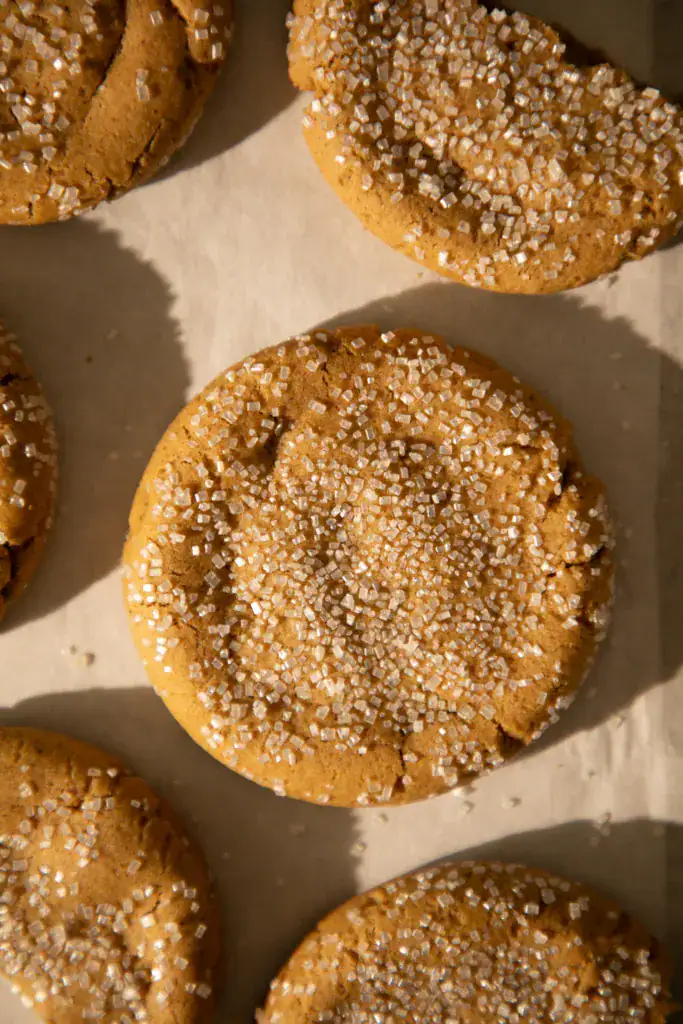 Soft and chewy ginger cookie topped with coarse sanding sugar cooling on parchment paper.