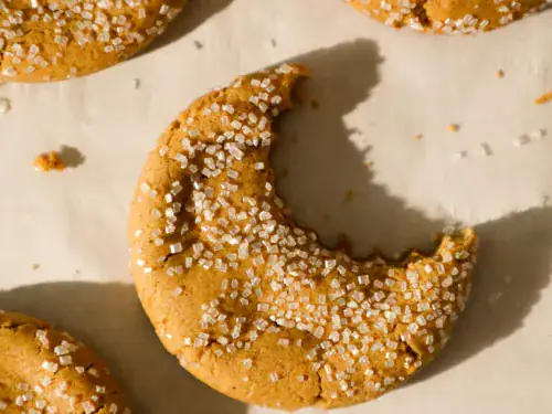 Chewy ginger cookie with coarse sugar topping and a bite missing, showing soft inside texture